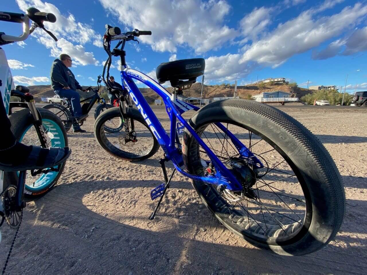 Blue electric bicycle parked on sandy ground.