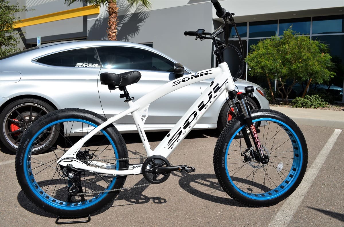 White bicycle with blue wheels near car.