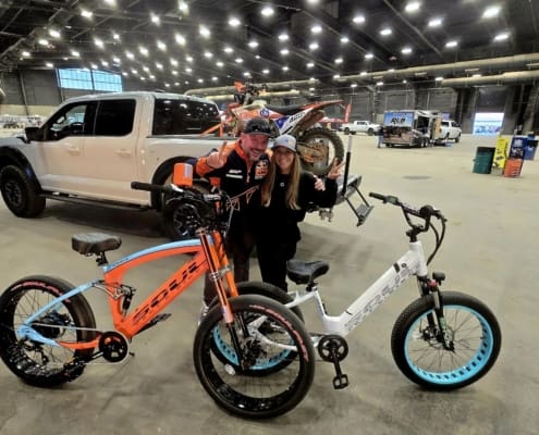 Two people posing with colorful bicycles indoors.