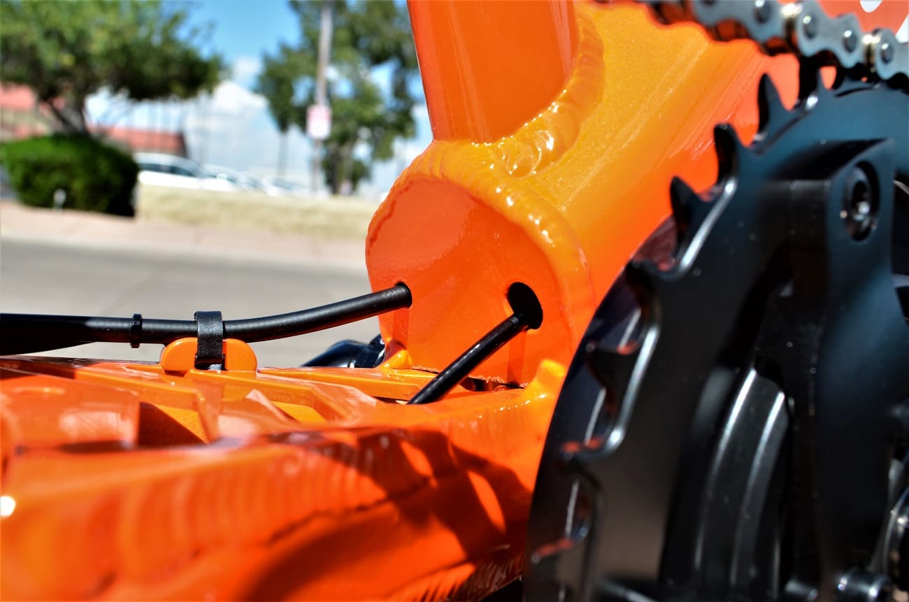 Orange bicycle frame with gear and cables.