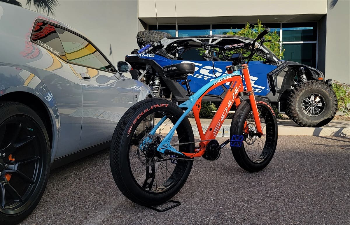 Orange and blue bike beside cars parked.