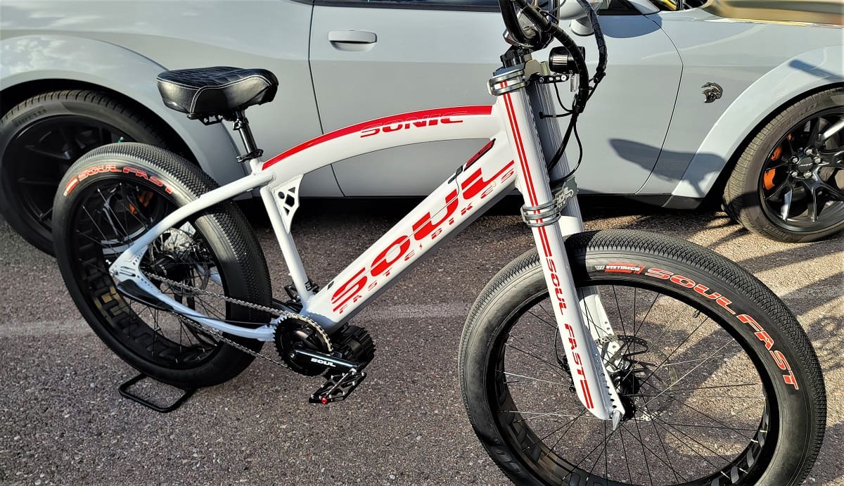 White and red bicycle beside a car.