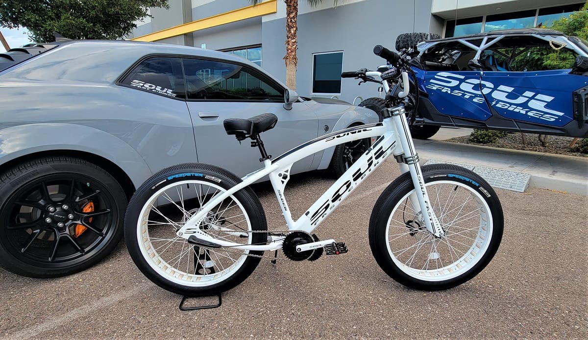 White bicycle parked beside a gray car.