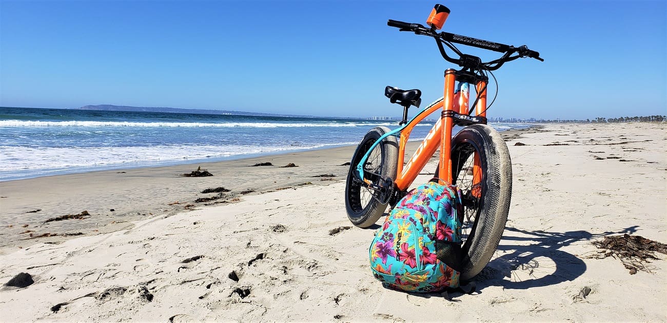 Orange bicycle on sandy beach with backpack.