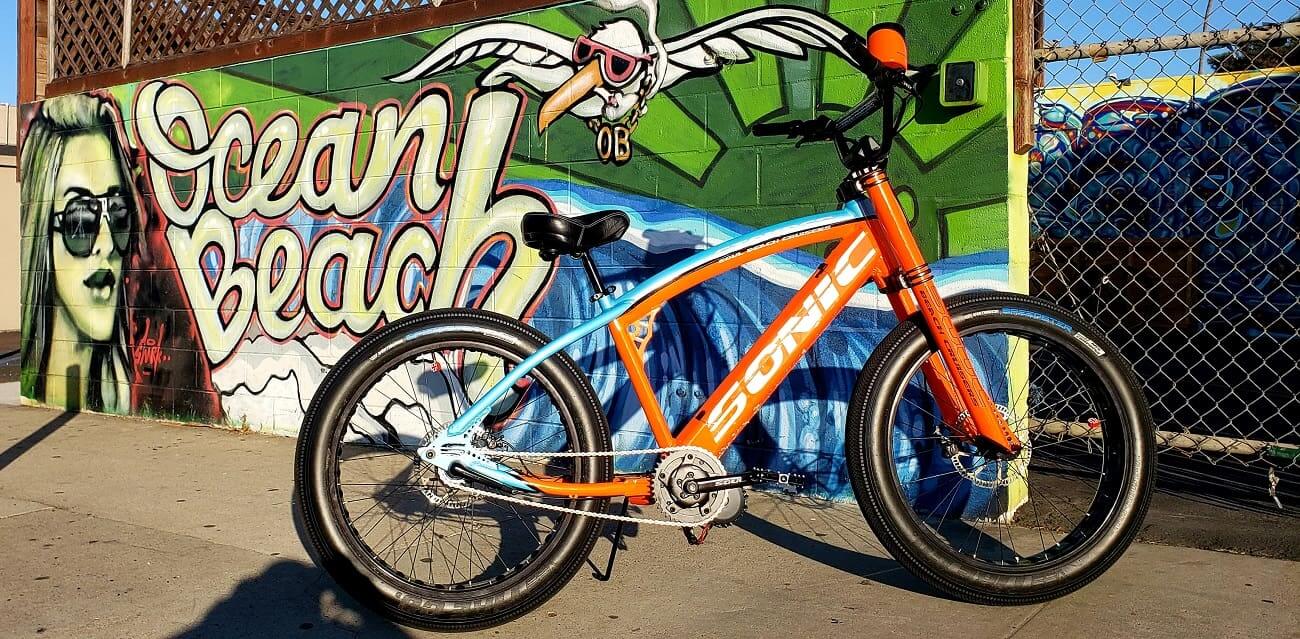 Orange bicycle in front of graffiti wall.
