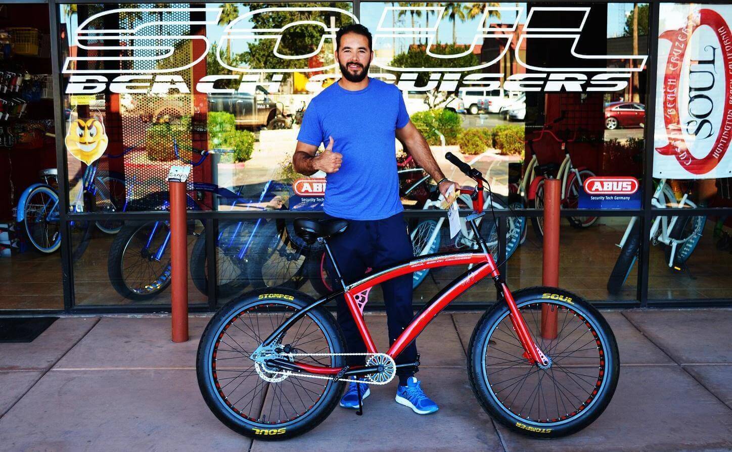 Man with red bicycle outside bike shop.