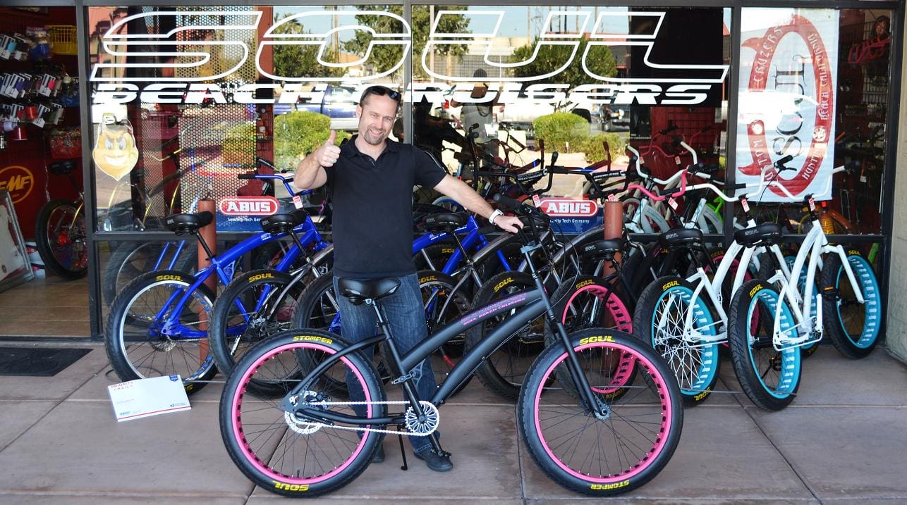 Man posing with bicycle outside shop.