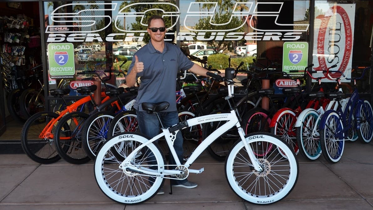 Man with bicycle outside bike shop.