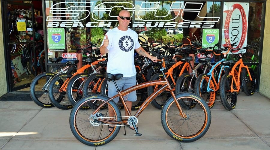 Man with bicycle outside bike shop.