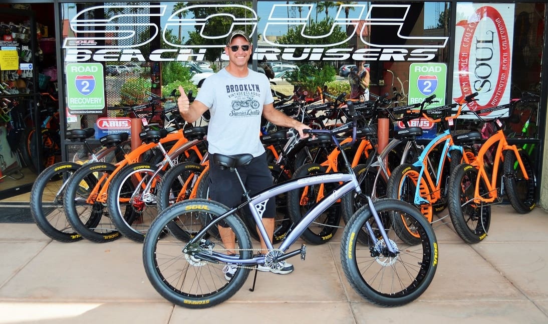 Man posing with bicycles outside a shop.