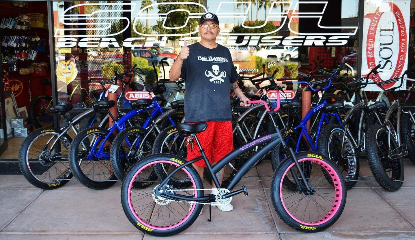 Man standing with bicycle outside bike shop.