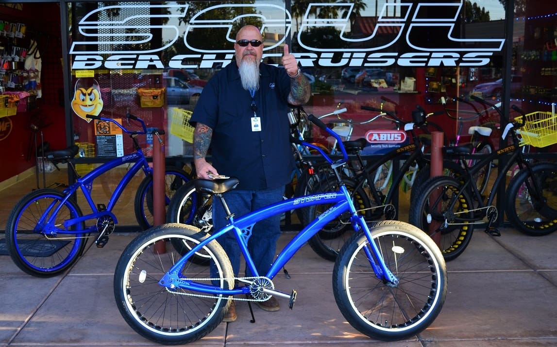 Man with bicycle outside bike shop.