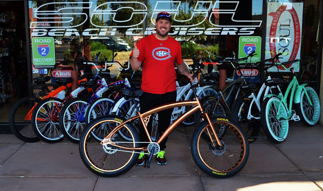 Man standing with a bicycle outside shop.