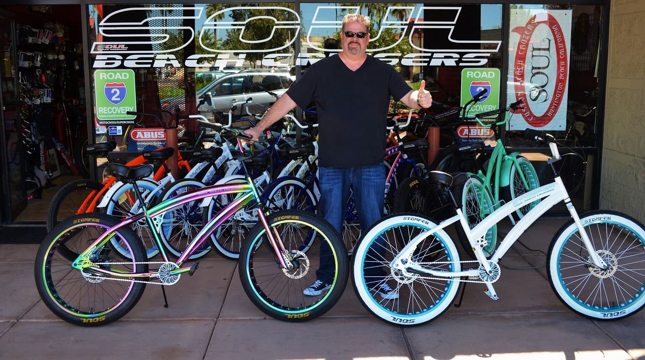 Man standing with colorful bicycles outside shop.