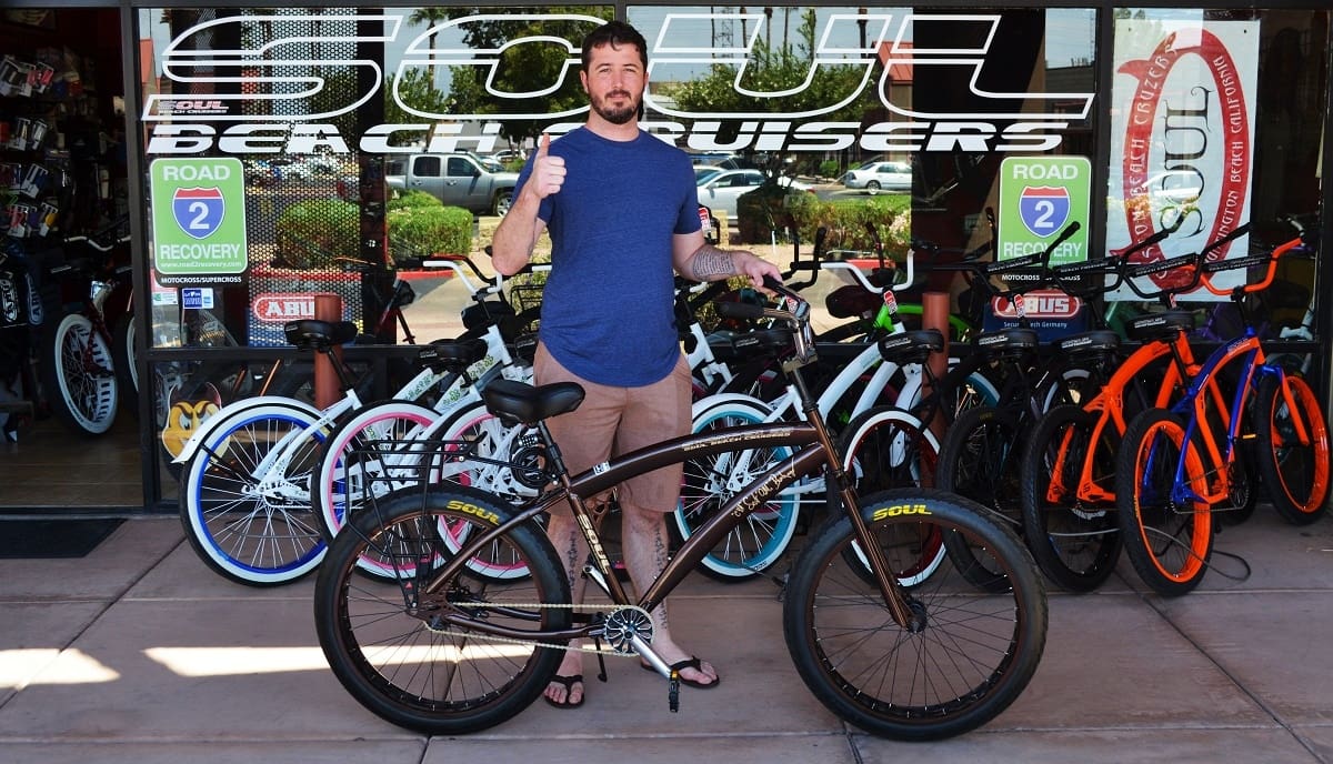 Man standing with bicycle outside bike shop.