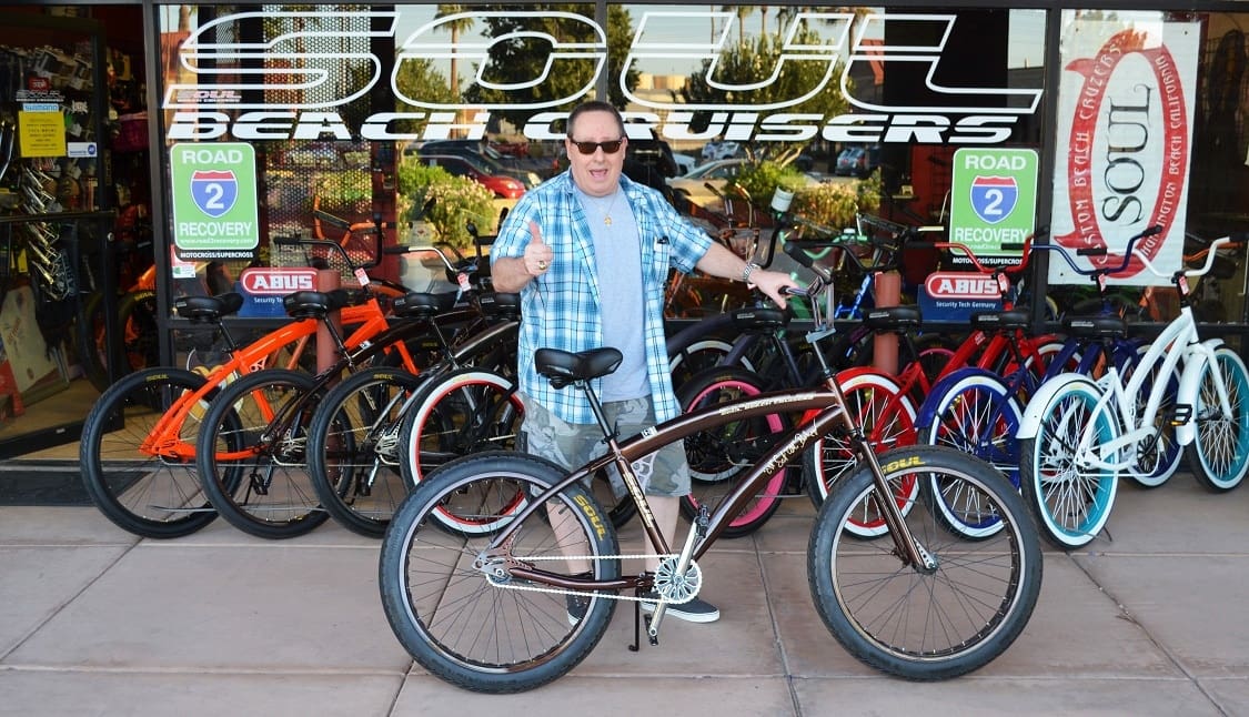 Man posing with bicycle outside bike shop.