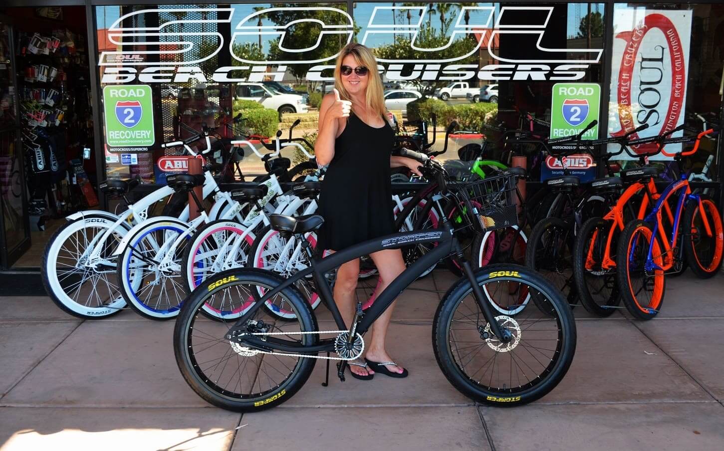 Woman posing with bicycle outside bike shop.