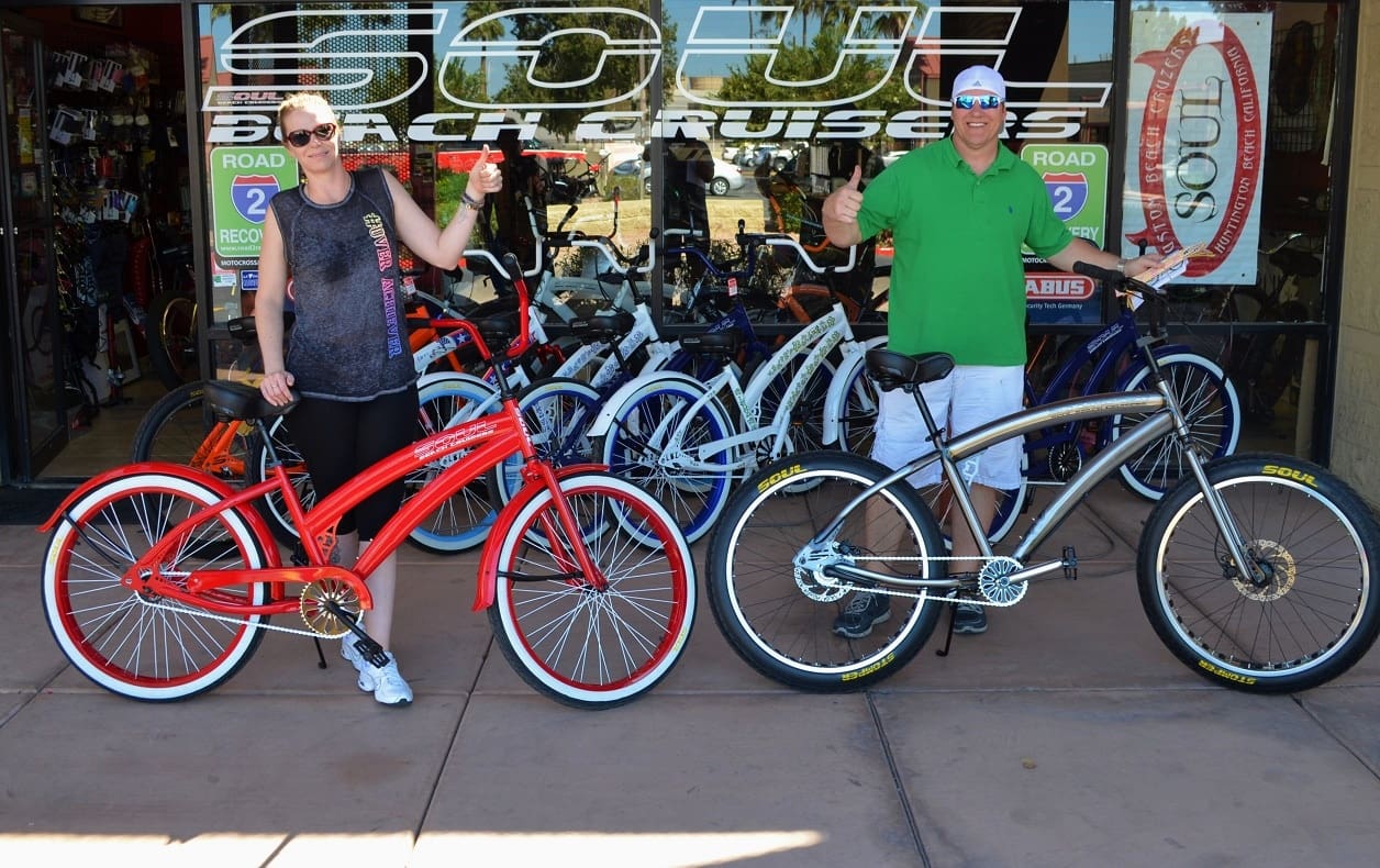 Two people posing with bicycles outside shop.