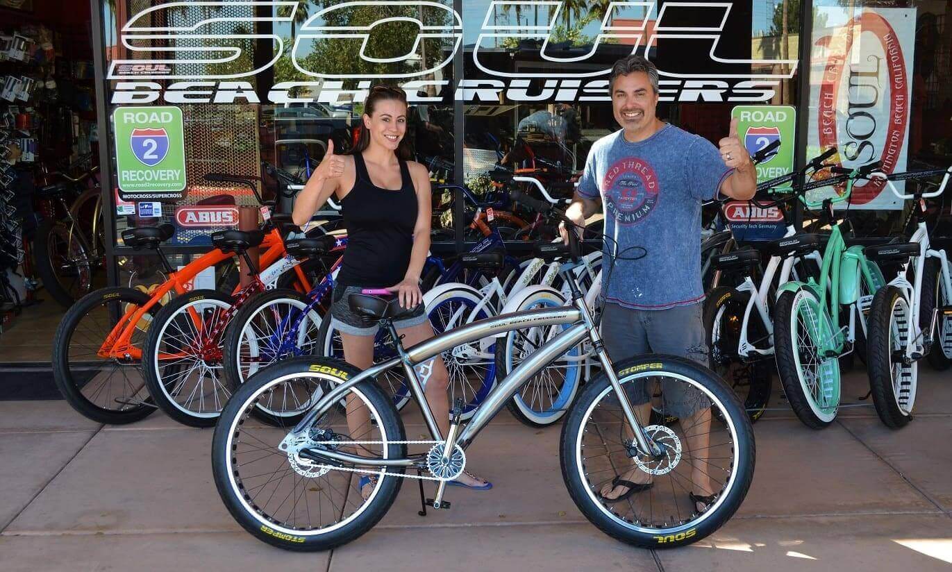 People smiling with bicycles outside shop.