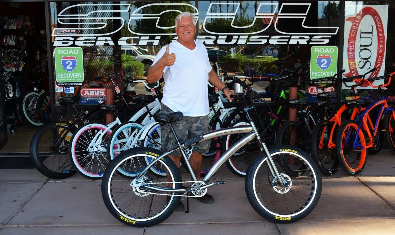 Man smiling with a bicycle outside shop.