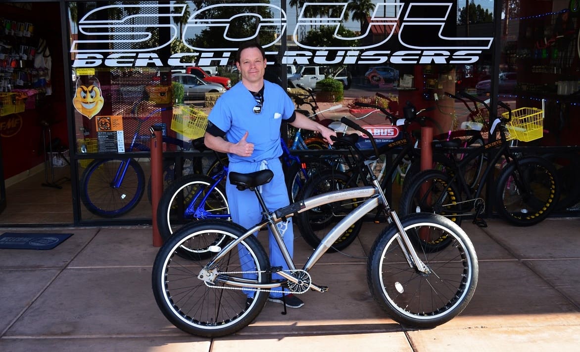 Man with bicycle outside shop, giving thumbs up.