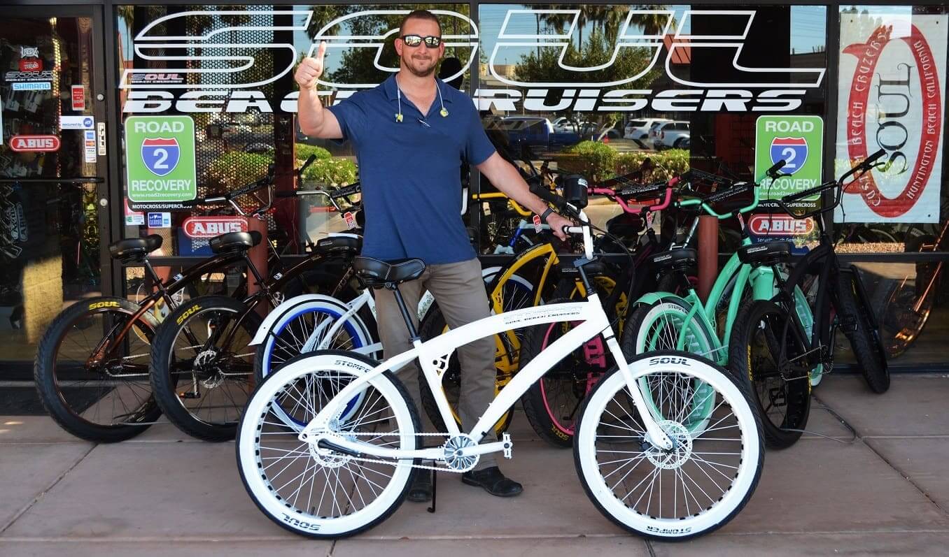 Man posing with white bicycle outside store.