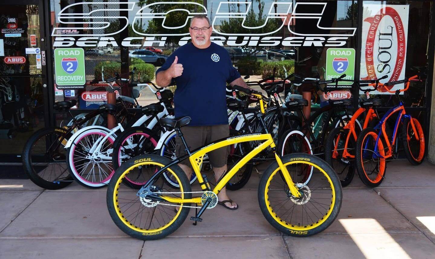 Man with yellow bike outside bicycle shop.