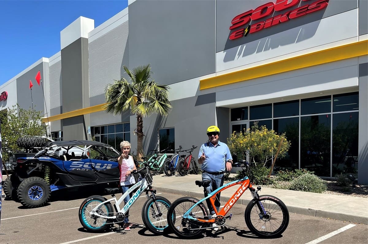 Two people with electric bikes outside store.
