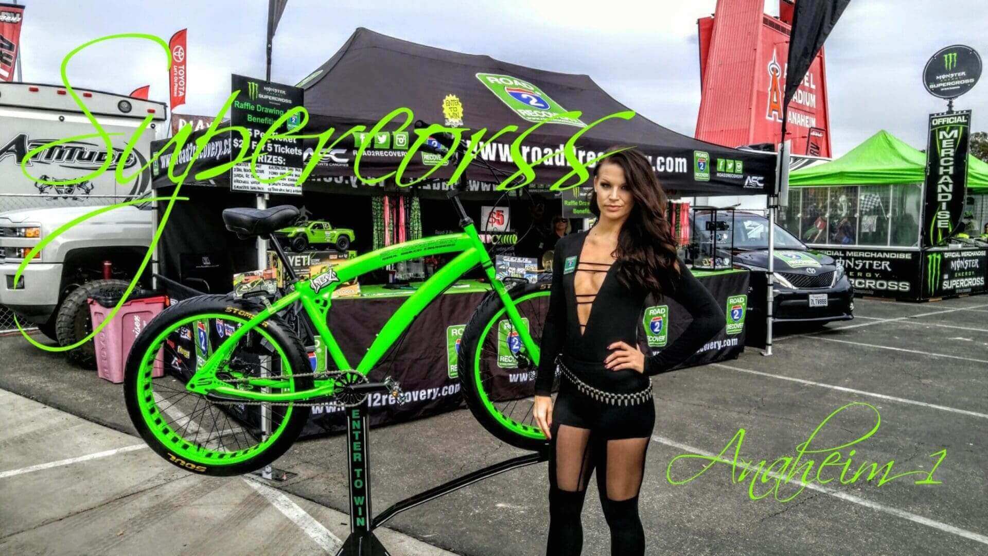 Woman posing by green bike, Supercross event.