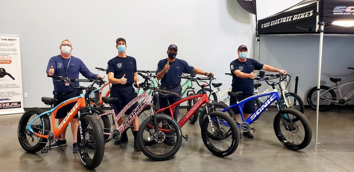 Four people with colorful electric bicycles indoors.