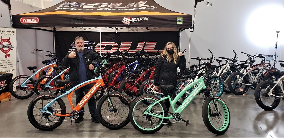 People posing with colorful bicycles in showroom.