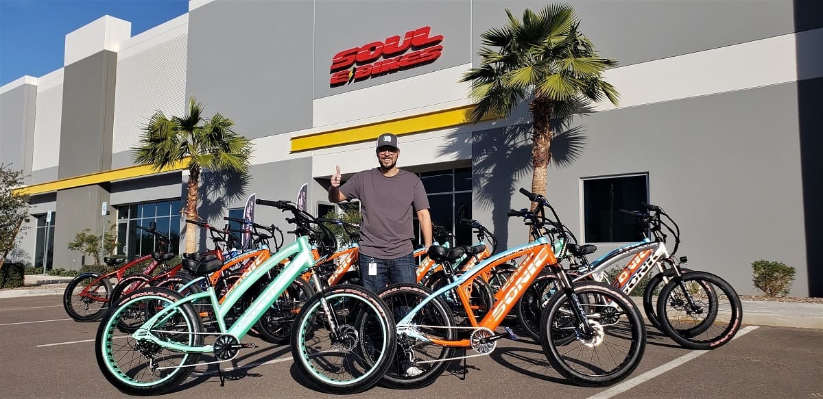 Man posing with colorful electric bicycles outside.