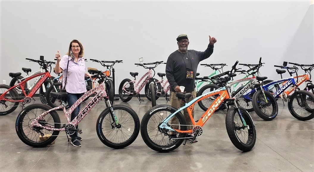 Two people with colorful electric bicycles indoors.