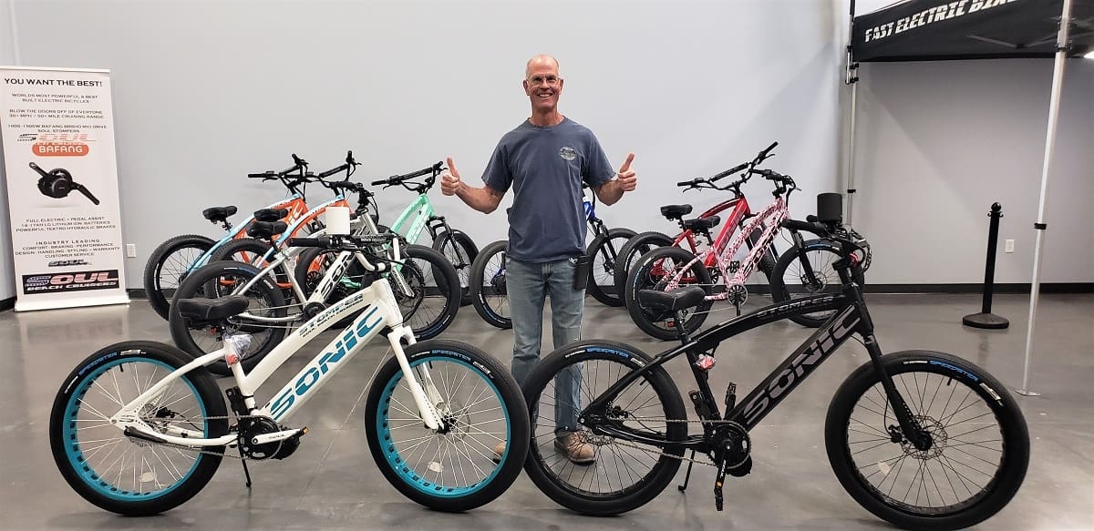Man posing with multiple electric bicycles indoors.