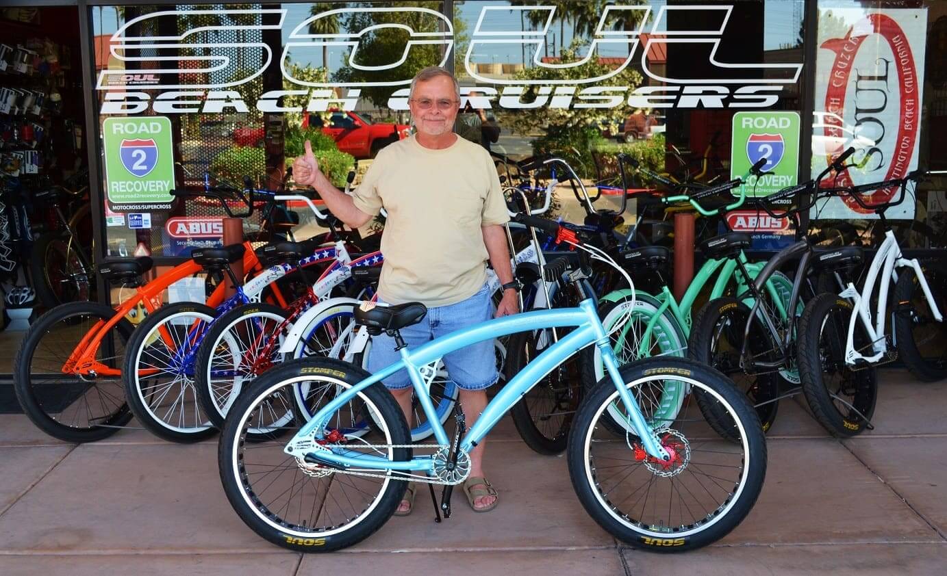 Man standing with bicycles outside bike shop.
