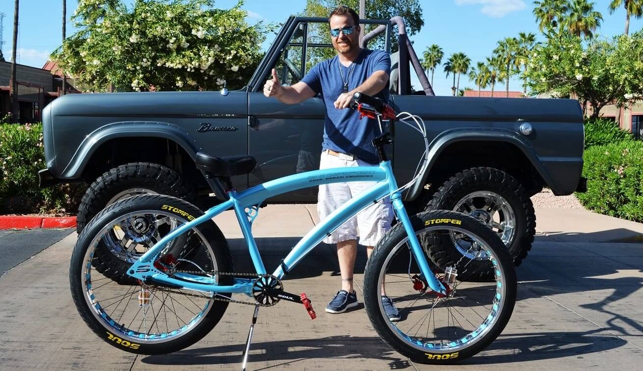 Man with blue bicycle and off-road vehicle.