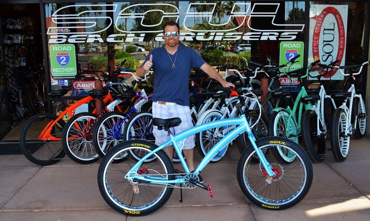 Man posing with beach cruiser bicycles outside.