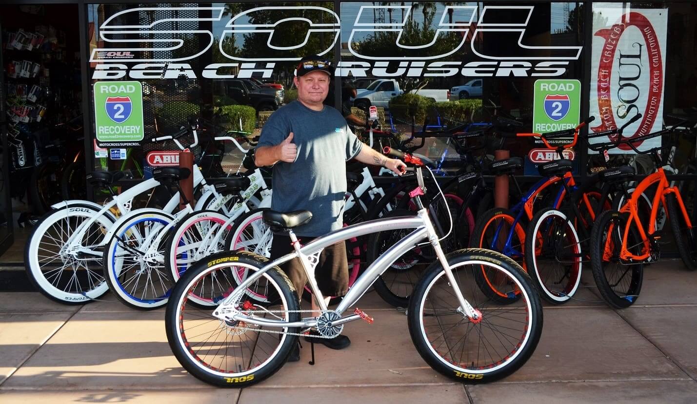 Man posing with bicycle outside bike shop.