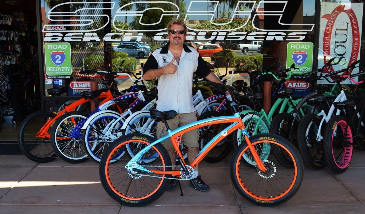 Man posing with colorful beach cruiser bikes.