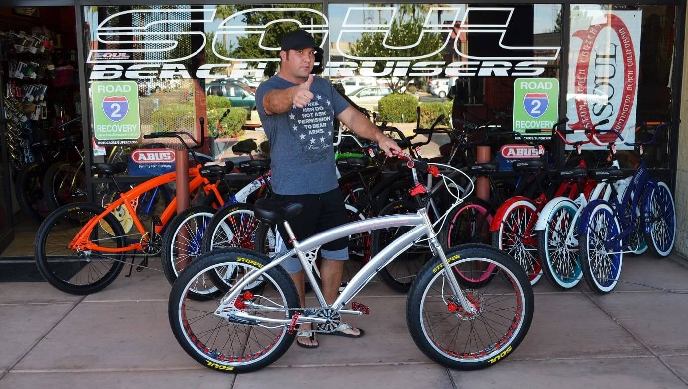 Man posing with bicycle outside bike shop.