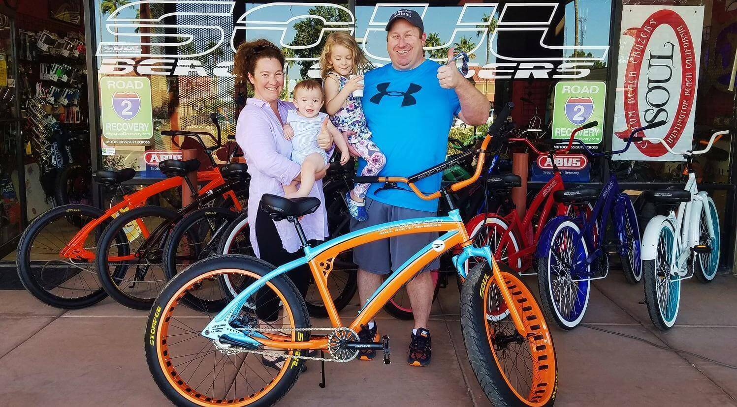 Family posing with colorful bicycles outside shop.