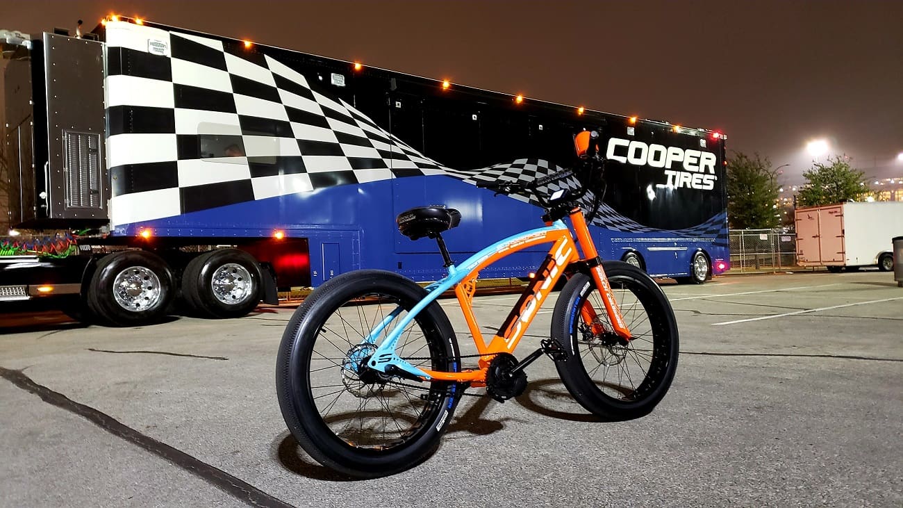 Orange bicycle beside a large racing truck.