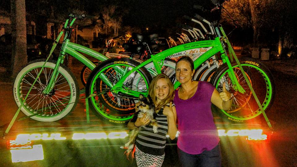 People posing with green bicycles at night.