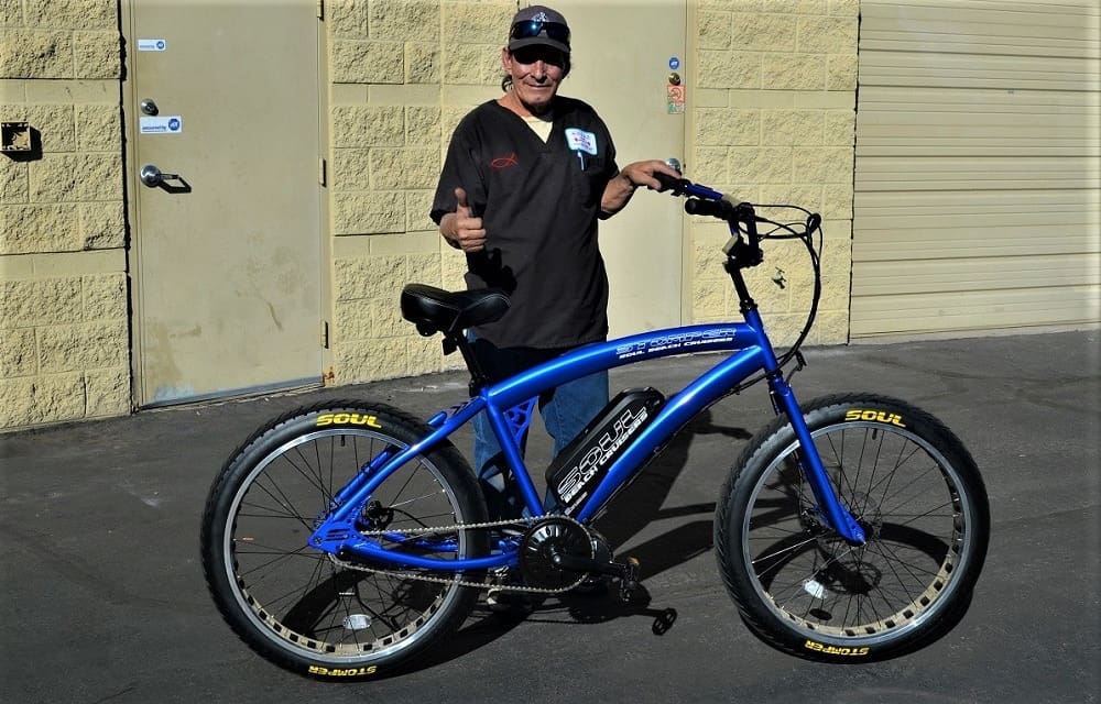Man posing with blue electric bicycle outdoors.