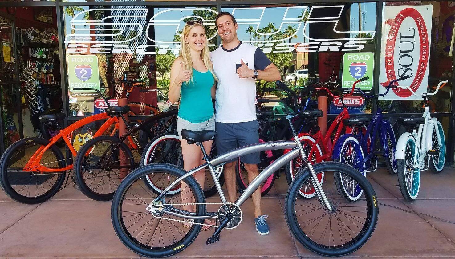 Couple posing with bicycles outside a shop.