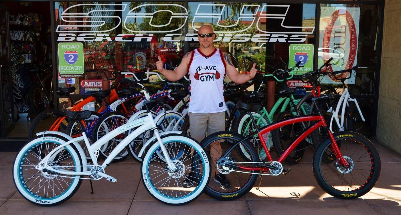Man posing with colorful beach cruiser bicycles.