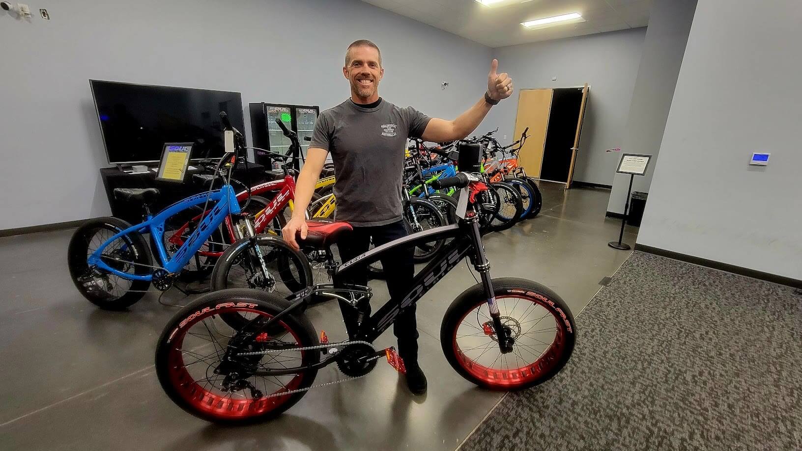 Man giving thumbs up with bicycle indoors.