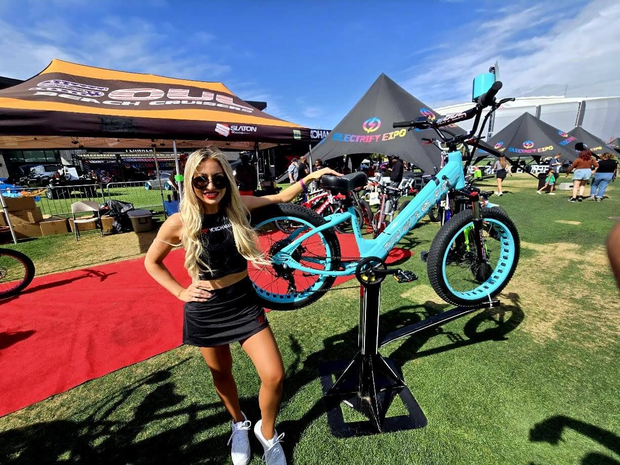Woman posing with turquoise bicycle at expo.
