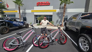 Man posing with custom bikes outside shop.