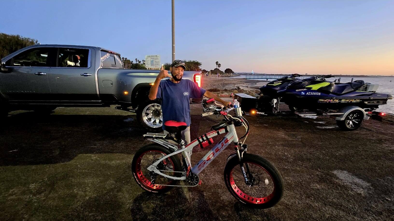 Man with bike near truck and jet skis.